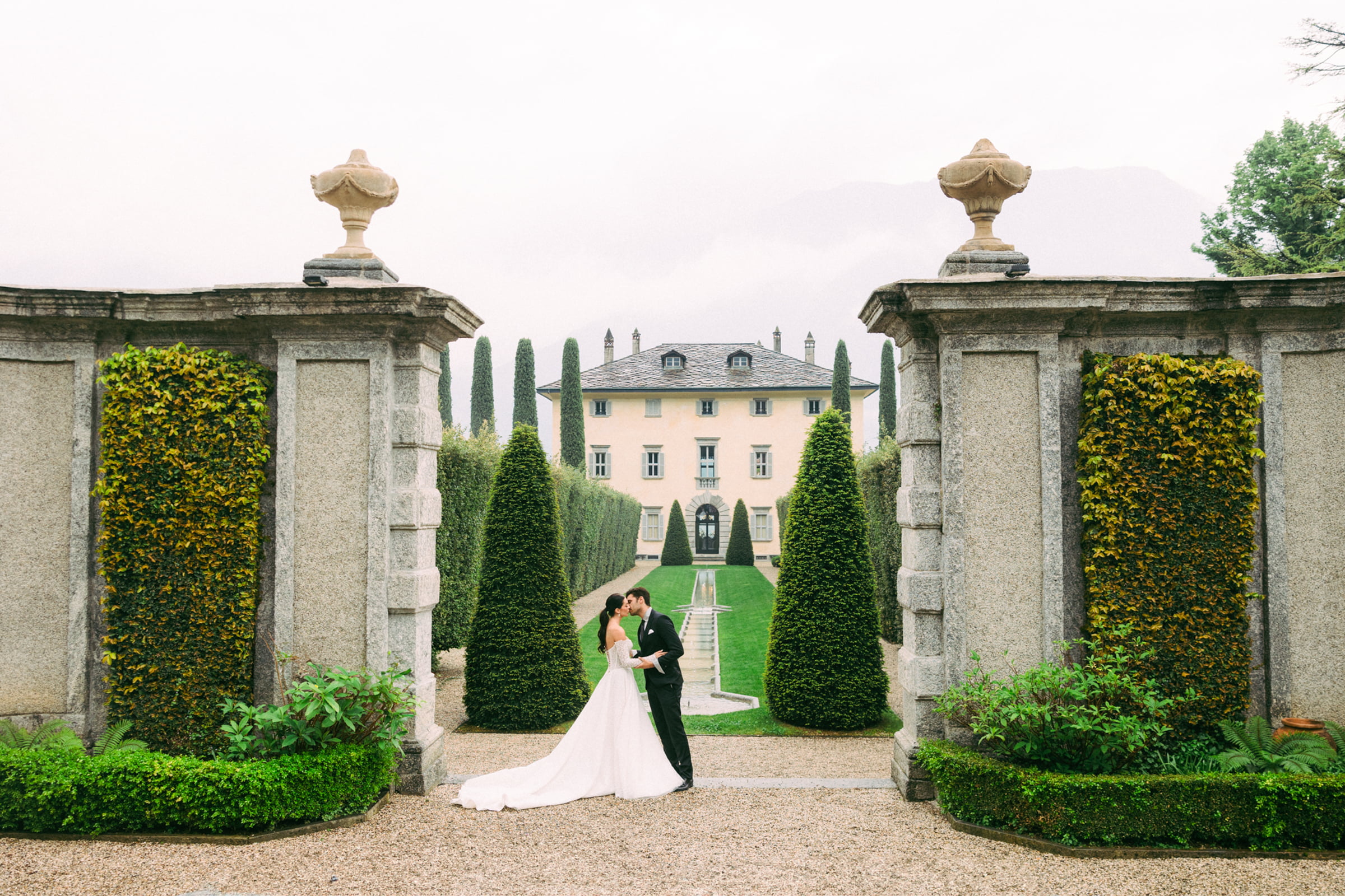 A wedding couple framed by stone gates and formal gardens at a villa