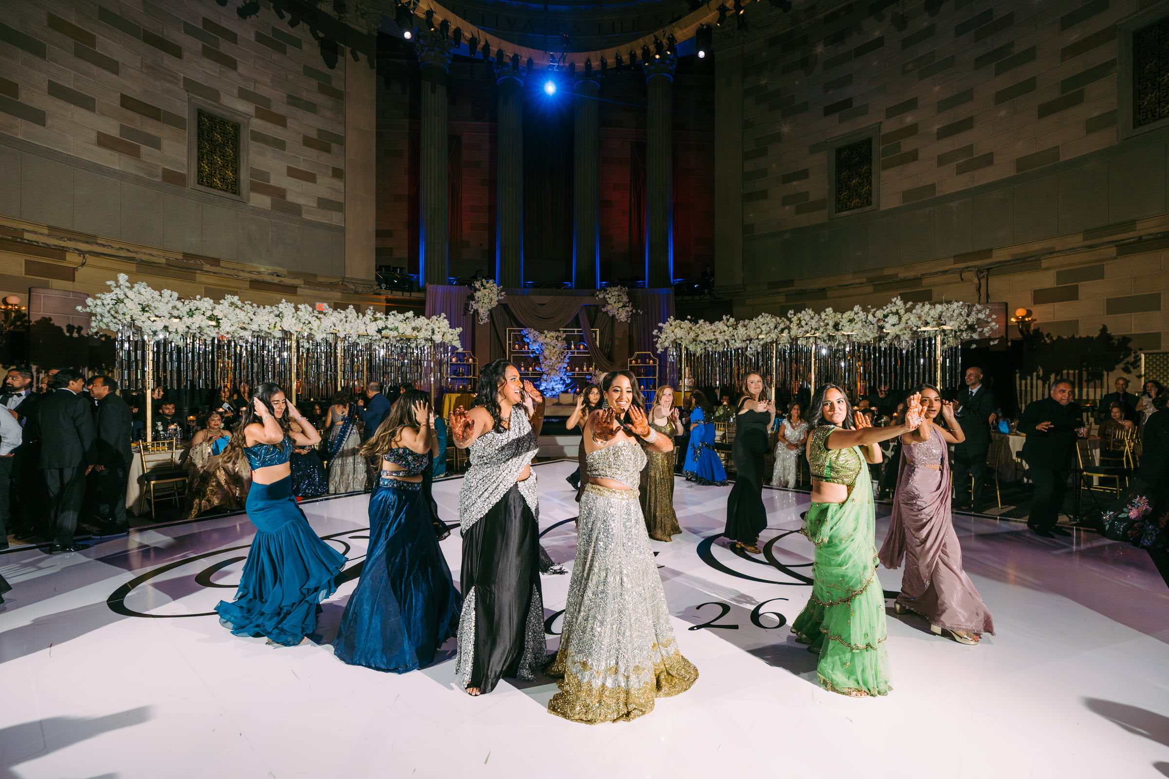 A bride and her friends dancing together in colorful wedding attire on a ballroom dance floor