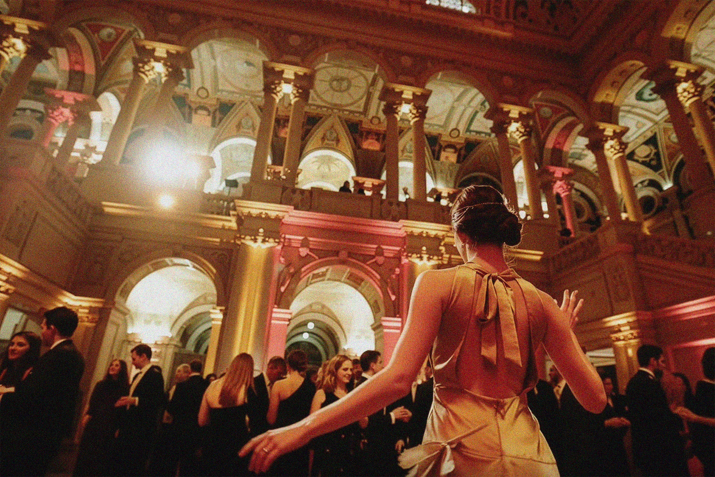 A guest dancing among friends in a warmly lit, ornate wedding reception hall
