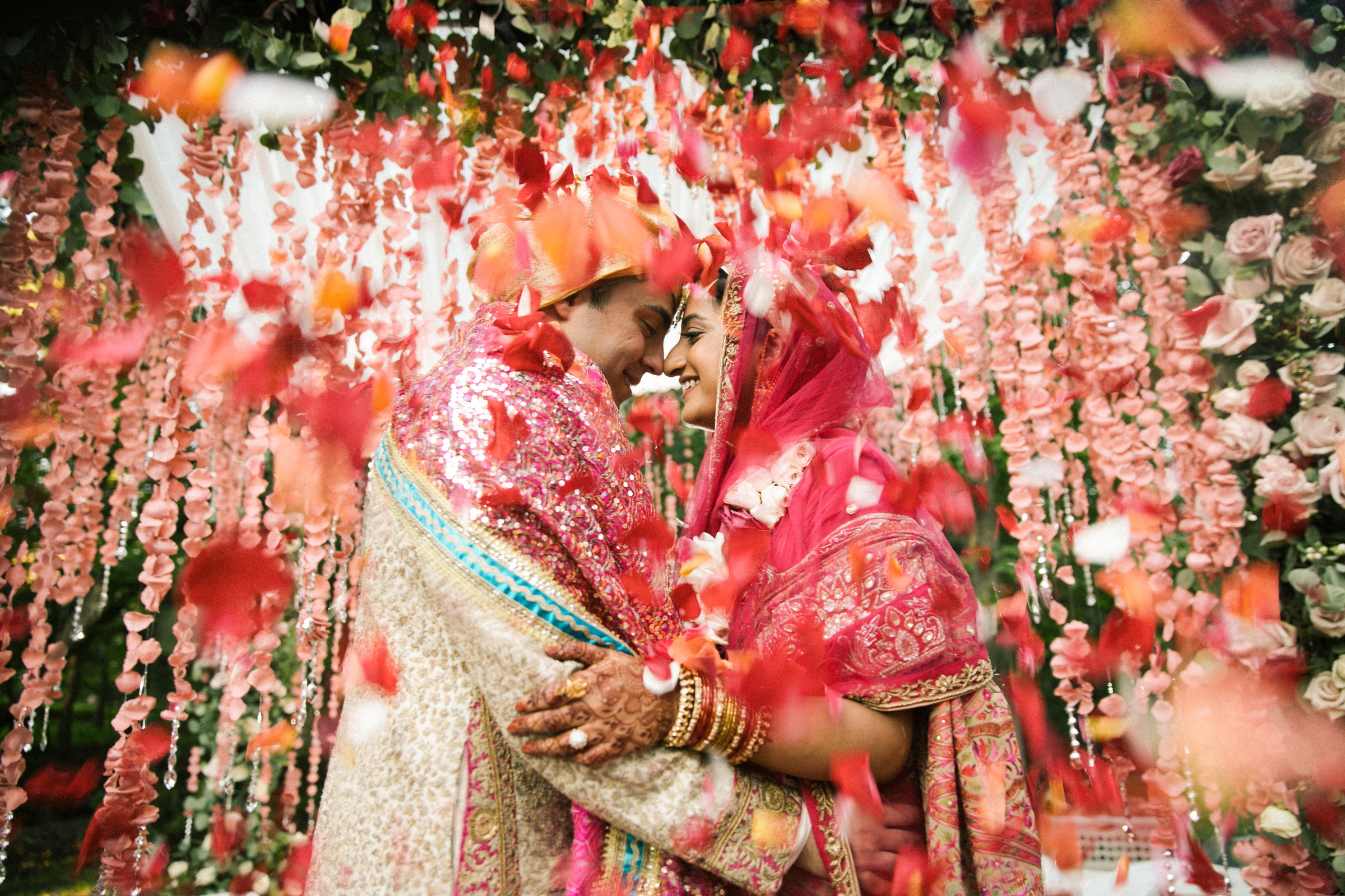 A newly married couple embracing as rose petals fall around them